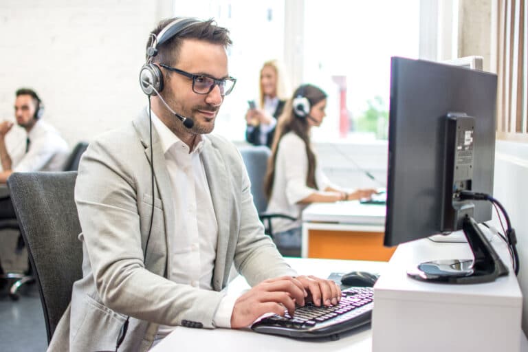 A man wearing glasses and a headset answers support requests on a computer